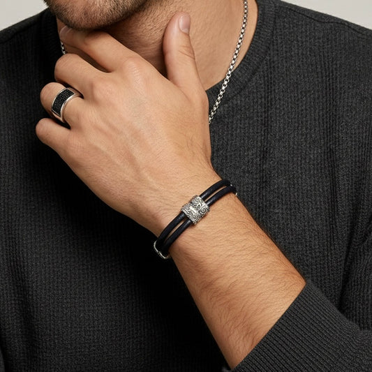 Man wearing a black leather bracelet with a silver clasp on his wrist, with a neutral background.