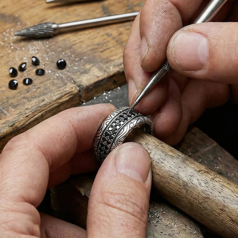 Close-up of hands working on a silver ring with tools and materials in the background